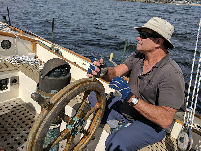 captain at the helm of a wooden sailboat