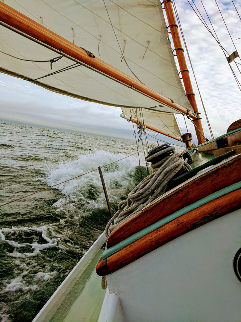 A classic wooden sailboat sailing under full sail on calm blue water.