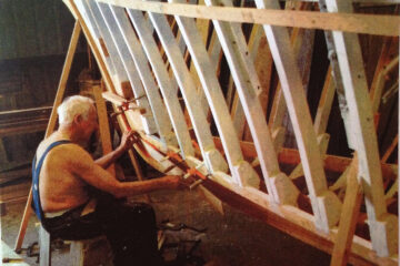 A craftsman shaping the wooden hull of a traditional boat during construction