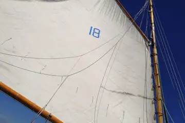 Close-up of a gaff‑rigged mainsail filled with wind against a blue sky