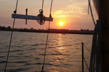 Sunset view from the deck of a classic sailboat with warm light on the water.