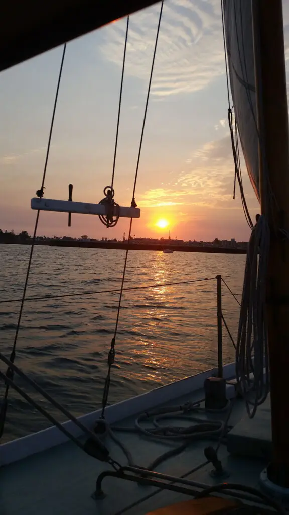 Sunset view from the deck of a classic sailboat with warm light on the water.