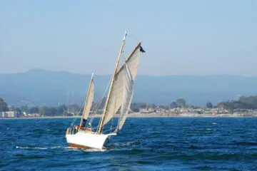 A yacht sailing away from the shoreline with mountains in the background.